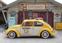 Gelber VW Käfer vor einer gestalteten Tankstellenkulisse im Retro-Stil
