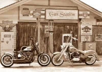 Drei Motorräder vor einer Gas-Station-Fassade im historischen Sepia-Look