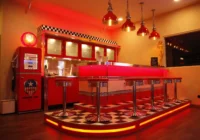 Massgefertigte rote Retro-Theke mit beleuchtetem Podest und Barhockern