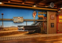 Grosses Route-66-Wüstenwandbild mit dem Heck eines schwarzen US-Oldtimers in einer Garage