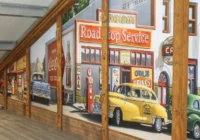 Gelber VW Käfer vor einer Café- und Road-Stop-Wandkulisse in einer Fahrzeughalle