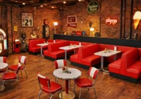 Rote Diner-Sitzbänke und Stühle vor Backsteinwänden mit Musikbox und Vintage-Schildern